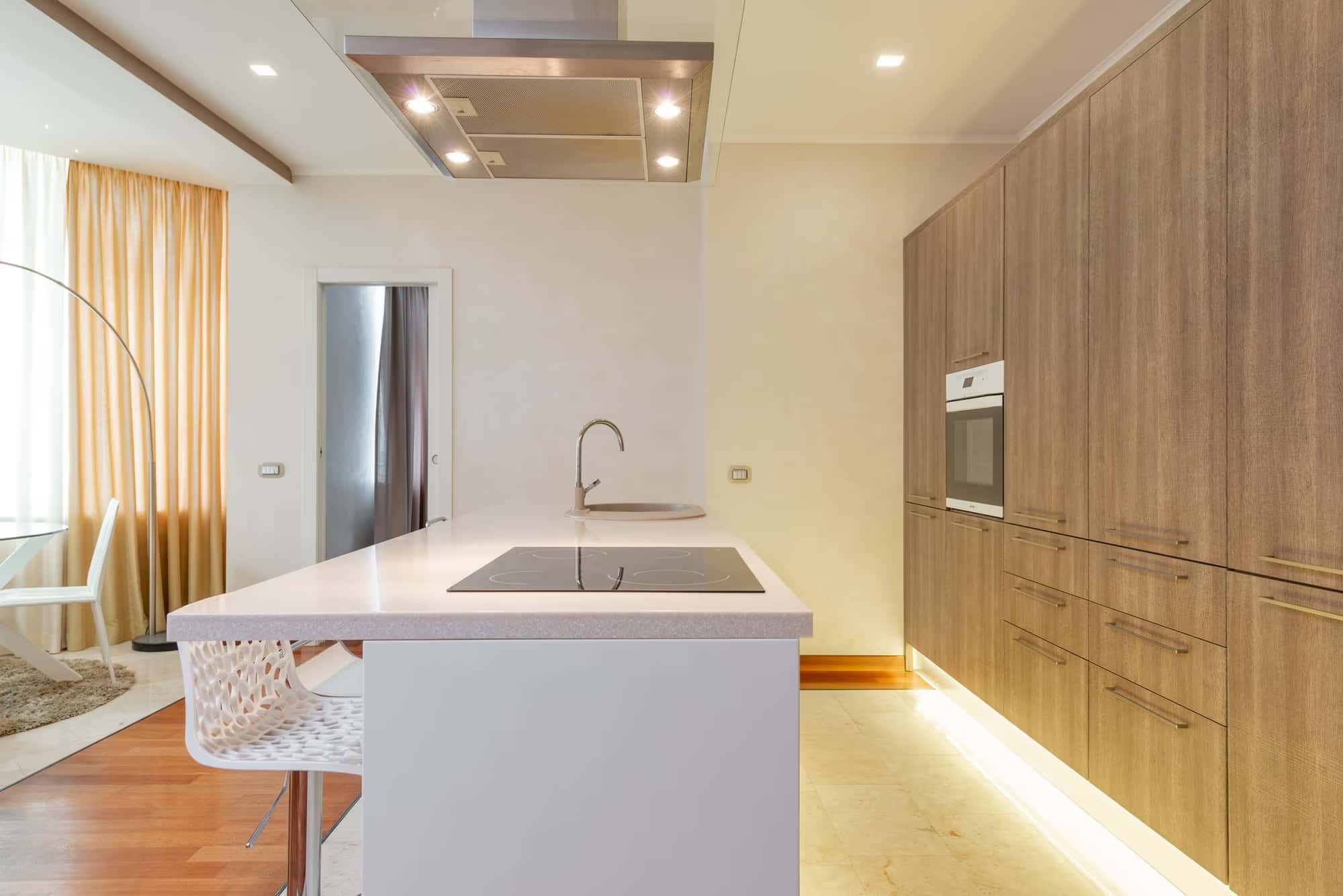 Minimalist kitchen renovation with white island, wood tall units and warm lighting